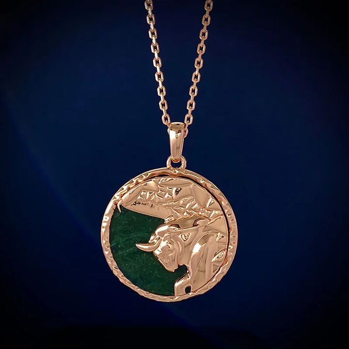 A gold zodiac necklace with a round pendant featuring an embossed bulls head on a green background, displayed against a dark blue backdrop—a striking piece of astrology jewelry.