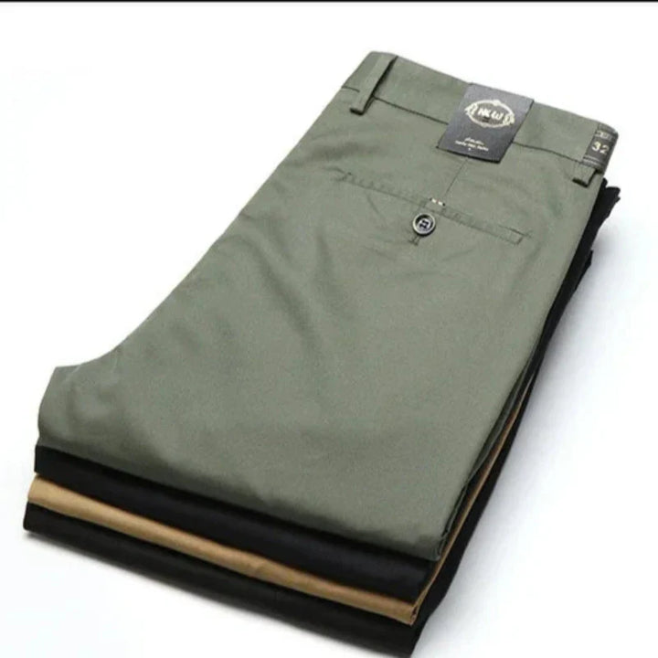 A stack of three neatly folded trousers in olive green, black, and khaki—each designed with a tailored fit and versatile style—displayed on a white surface. A tag is attached to the top green pair.