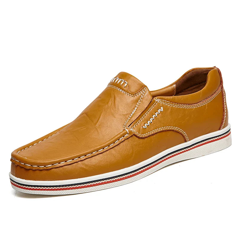A light brown boat-style loafer crafted from leather with white stitching, a white sole, and red and black accent stripes along the edge of the sole.