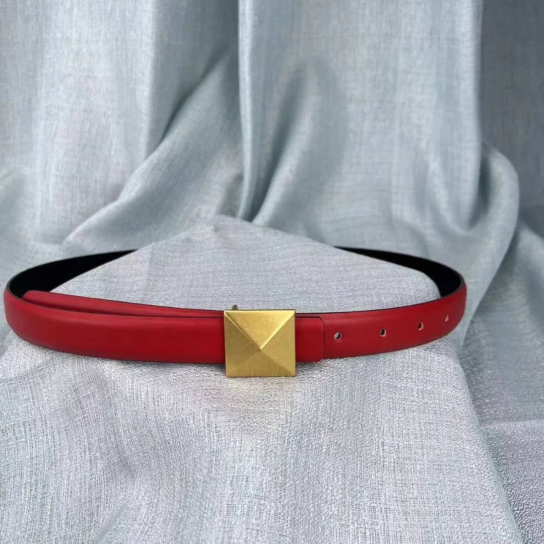A red leather belt with a large square gold buckle is displayed on a light gray textured fabric backdrop, featuring an adjustable length for the perfect fit.