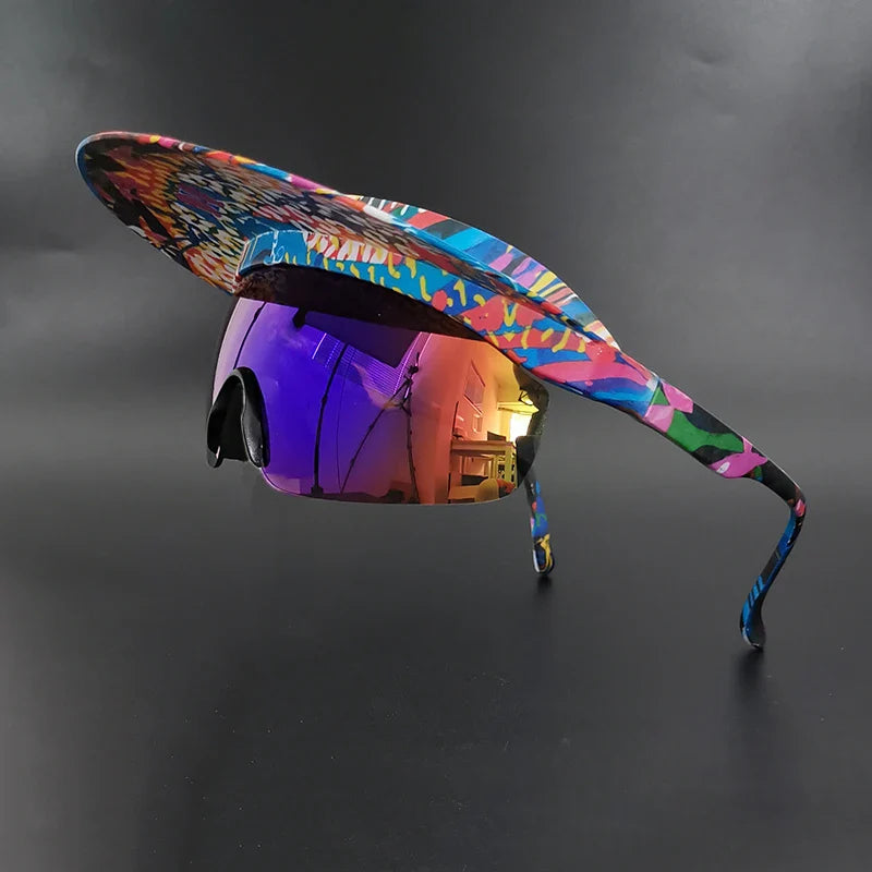 A colorful, abstract-patterned visor with large reflective sunglasses attached offers UV400 protection and panoramic visibility. Displayed against a solid black background, the bold, futuristic design blends visor and sunglasses seamlessly.