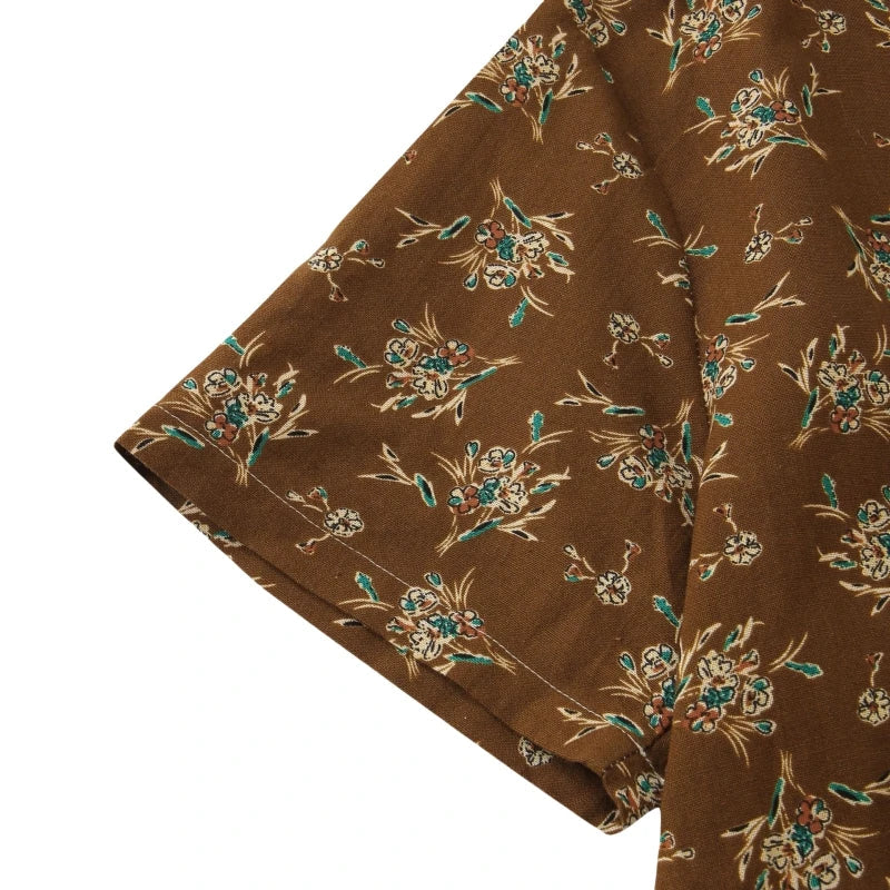 Close-up of a brown short-sleeve cotton shirt with a floral pattern in light blue, beige, and green tones. The fabric appears soft and lightweight, featuring a relaxed fit and classic design for easy, casual style.