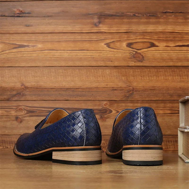 A pair of blue luxury footwear with a basketweave pattern and light brown soles, crafted from real leather, displayed on a wooden surface with a wood-paneled background. The shoes are positioned with the heels facing forward.