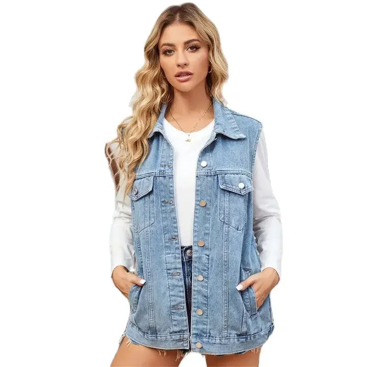 A woman with long, wavy blonde hair wears a sleeveless denim vest made from lightweight breathable fabric over a white long-sleeve shirt and denim shorts, standing with her hands in the vest pockets against a plain white background.