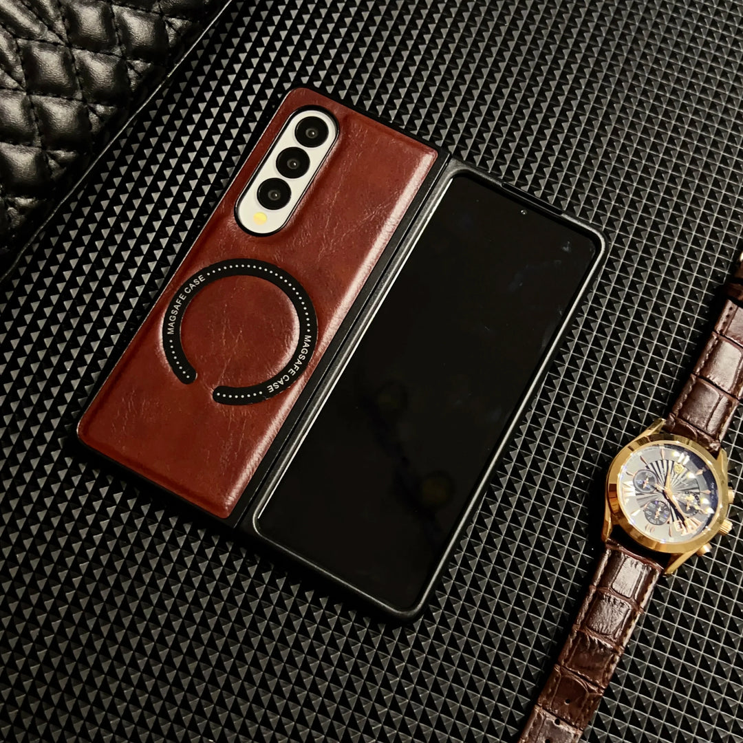 A foldable smartphone with a brown Samsung Galaxy Z Fold case and ring holder rests on a textured black surface beside a brown leather-strapped gold watch.