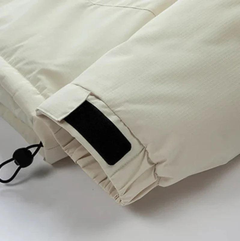 Close-up of the sleeve of a light beige windproof jacket, featuring a black Velcro strap for adjusting the cuff and a black drawstring with a plastic toggle at the hem.