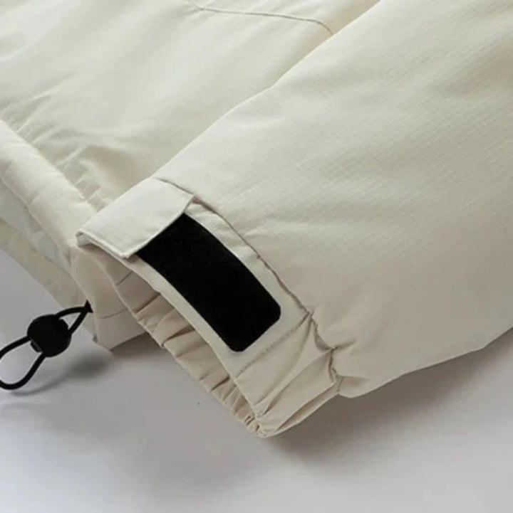 Close-up of the sleeve of a light beige windproof jacket, featuring a black Velcro strap for adjusting the cuff and a black drawstring with a plastic toggle at the hem.