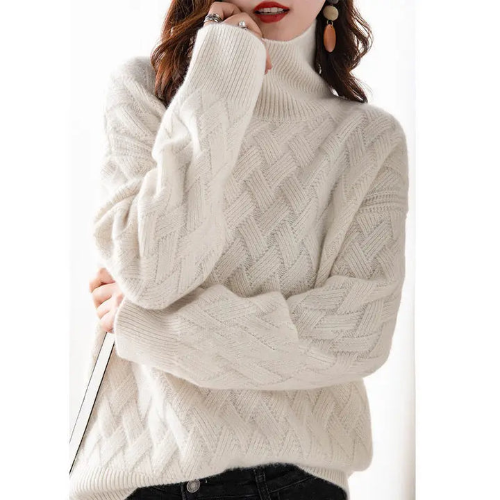 A woman wears an ultra soft, white cashmere blend turtleneck sweater with a textured knit pattern and long sleeves, paired with black pants. Her wavy brown hair and dangling earrings complete the look as she crosses her arms casually.
