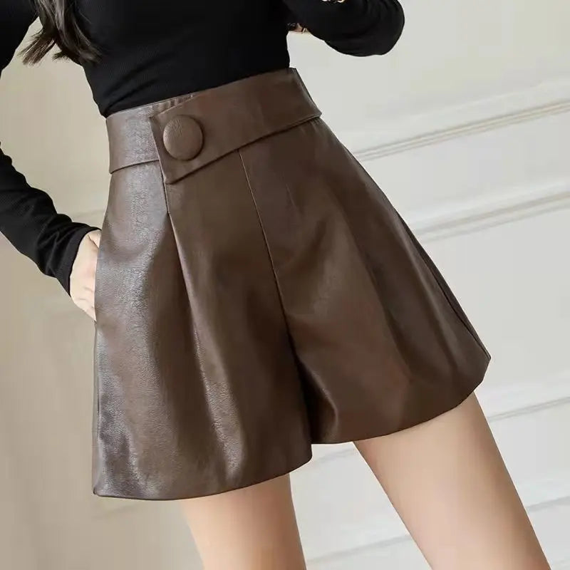 A person wearing high-waisted, brown faux leather shorts with a wide waistband and stylish button detail, paired with a black long-sleeve top.