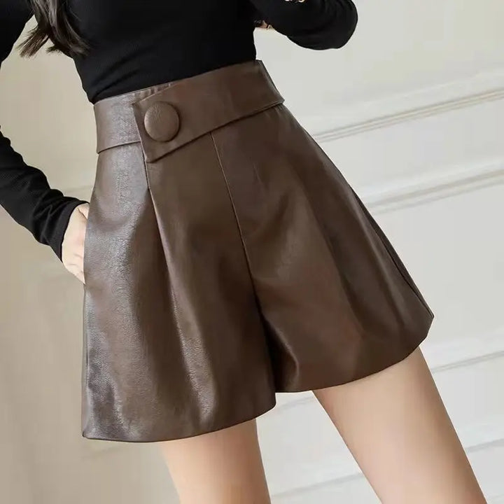 A person wearing high-waisted, brown faux leather shorts with a wide waistband and stylish button detail, paired with a black long-sleeve top.