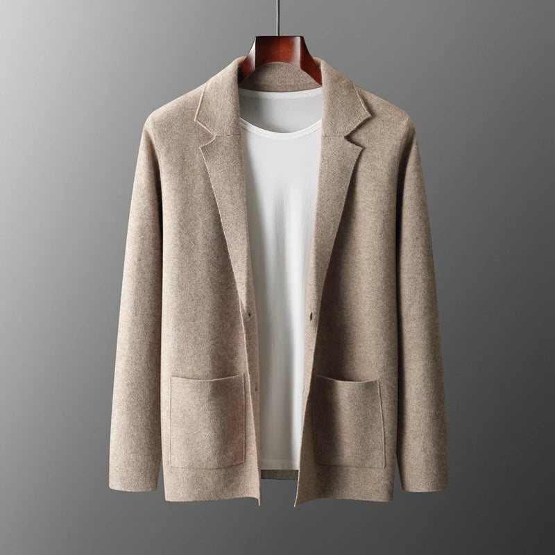 A beige blazer with two front pockets is displayed on a hanger over a plain white t-shirt, paired for a business casual cardigan look, set against a neutral gray background.