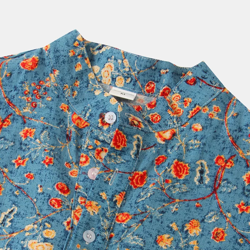 Close-up of a blue cotton shirt with a vibrant red and orange floral pattern, white buttons, and a mandarin collar—a classic design displayed against a white background.