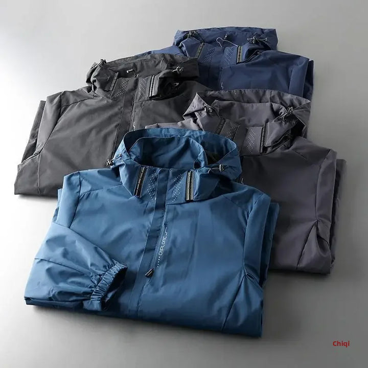 Four folded hooded jackets in shades of blue, gray, and black are neatly arranged on a flat surface, showcasing their zippers and front pockets—each designed as a breathable outdoor jacket for comfort and performance.