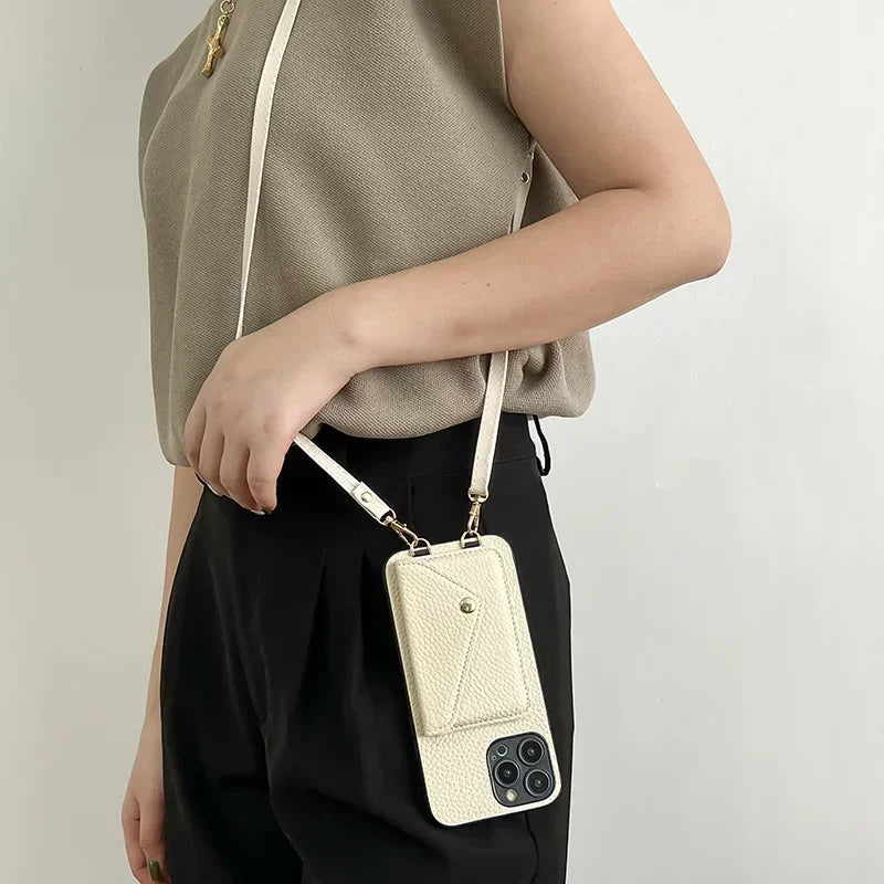 A person wearing a beige top and black pants carries a cream-colored phone case with a strap over their shoulder. The case, made from pebble-texture material, features a small cardholder pocket with a snap button.