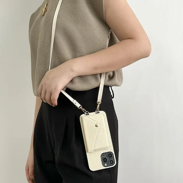 A person wearing a beige top and black pants carries a cream-colored phone case with a strap over their shoulder. The case, made from pebble-texture material, features a small cardholder pocket with a snap button.