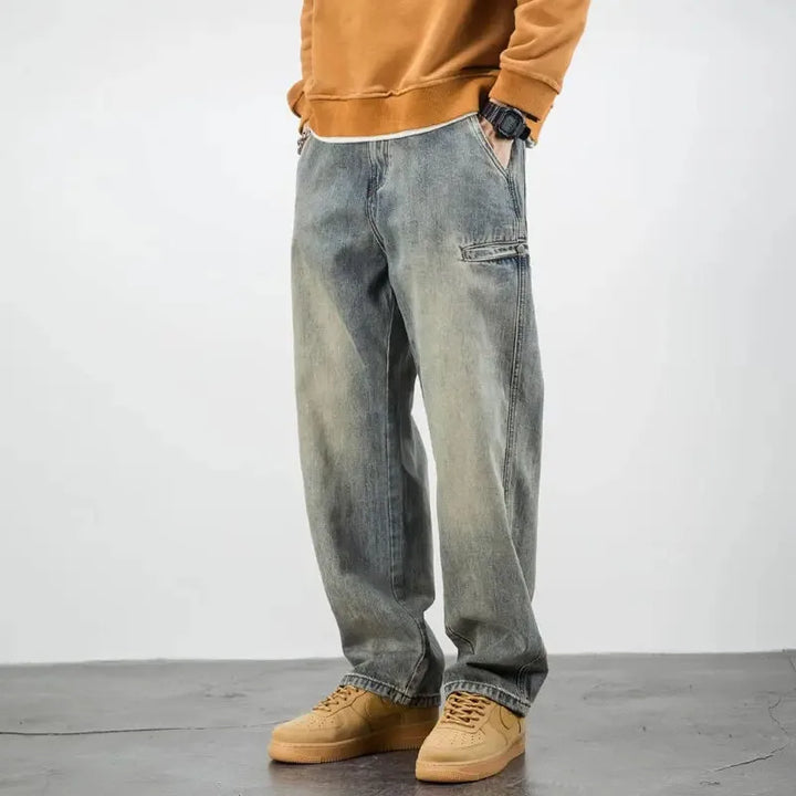 A person wearing a brown sweatshirt, classic straight leg stone washed jeans, and tan sneakers stands with hands in pockets against a plain light background. Their face is not visible.