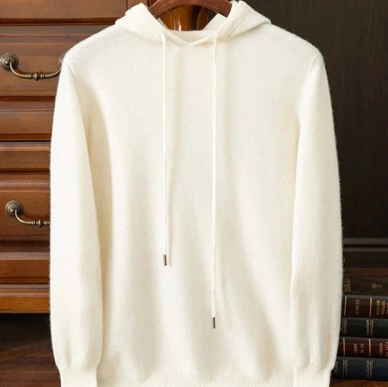 A plain white layering sweater with drawstrings is displayed on a hanger, set against a wooden background and a stack of books.