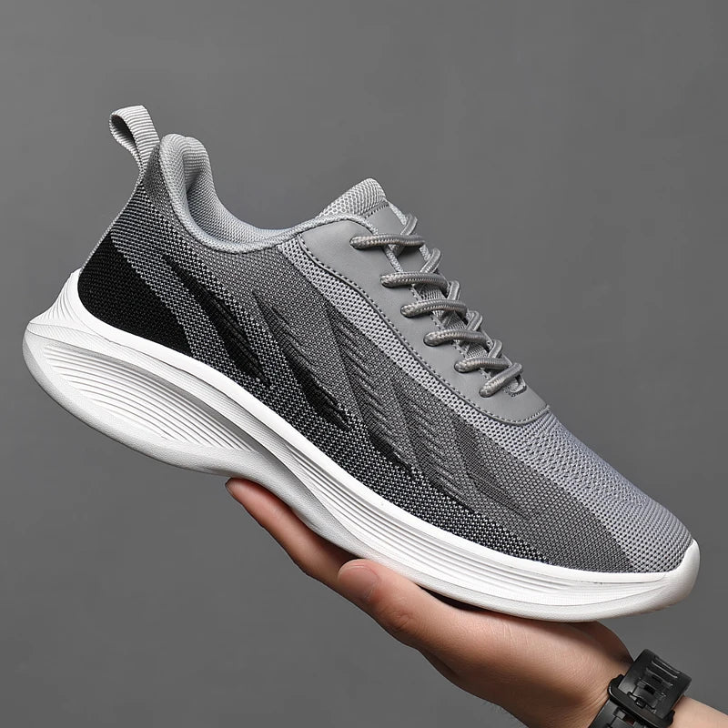 A hand holds up a stylish gray athletic sneaker with black accents, a breathable mesh upper, excellent arch support, and a thick white sole against a plain gray background.