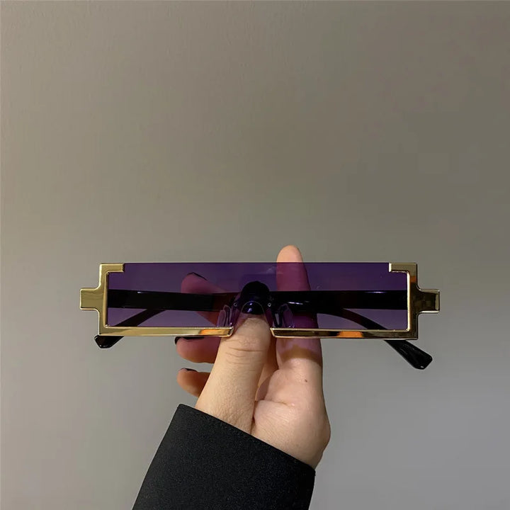 A hand holds a pair of rectangular sunglasses with purple lenses and gold geometric frames, featuring UV400 protection, against a plain gray background.