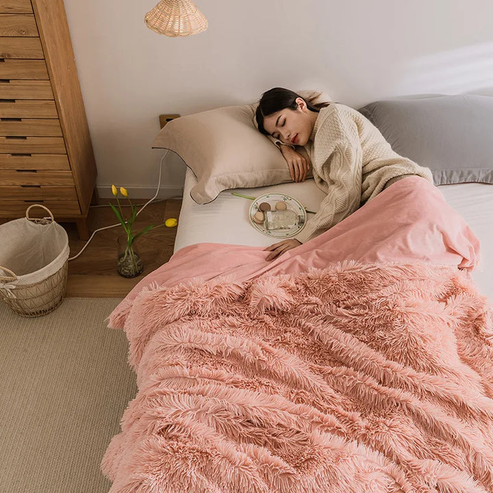 A woman in a cozy sweater sleeps on a bed with a Soft Faux Fur Throw Blanket. A tray with snacks and a drink rests beside her, while a basket with yellow tulips sits on the floor, creating a warm and cozy atmosphere.