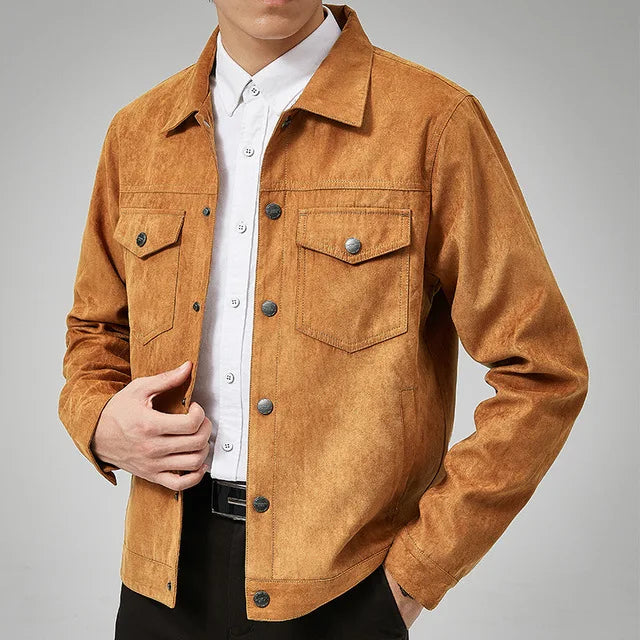 A person in a light brown suede jacket with classic point collar over a white button-up shirt and black pants, one hand lightly holding the jacket near the chest. The face is partially out of frame.
