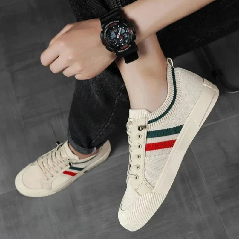 A person wearing cream-colored sneakers with green and red stripes and a durable rubber outsole, paired with black jeans. The look is completed with a black digital wristwatch, all seen from above.