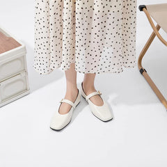 A person wearing a white, polka-dotted skirt and cream-colored sheepskin ladies shoes stands on a white floor near a beige foldable chair and a white storage box.