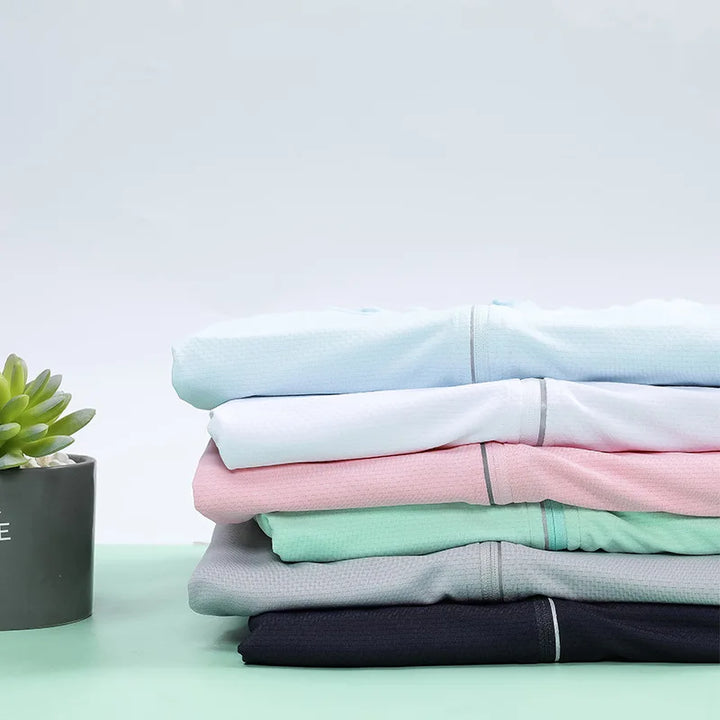 A neatly folded stack of pastel-colored, quick-drying fabric clothes sits on a mint green surface next to a gray pot with a small green succulent. The background is plain and light-colored.