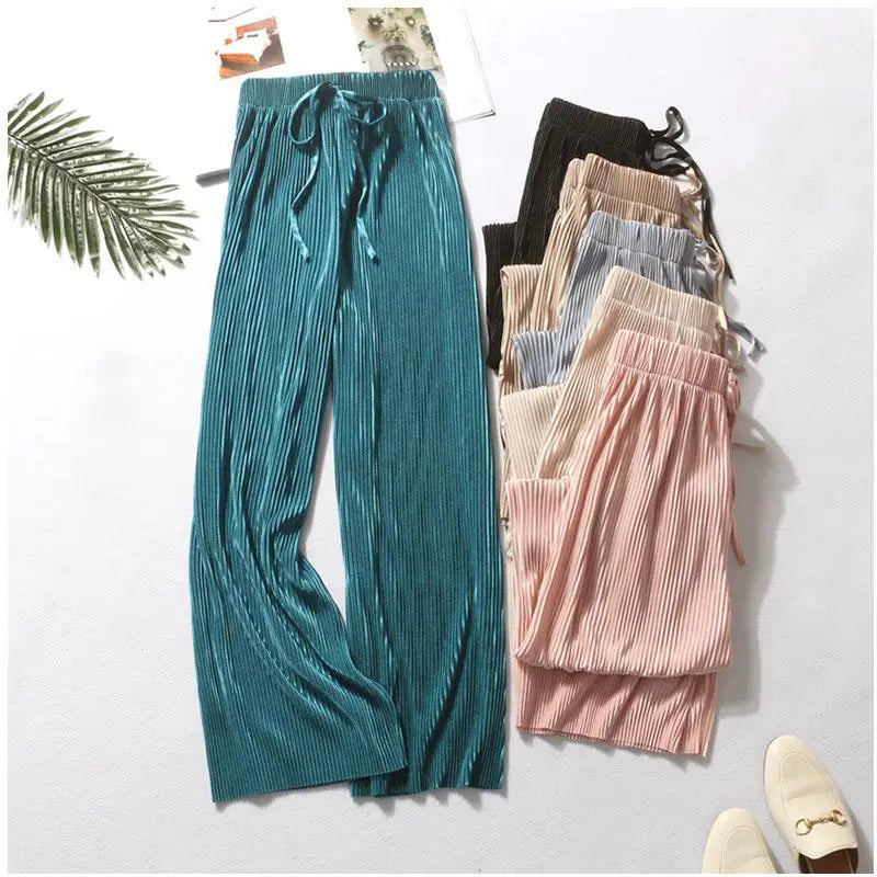 A variety of Pleated Ice Silk wide-leg pants in teal, brown, gray, beige, and pink are laid out neatly on a white surface next to a green leaf and a pair of cream loafers—perfect for women fashion summer pants.