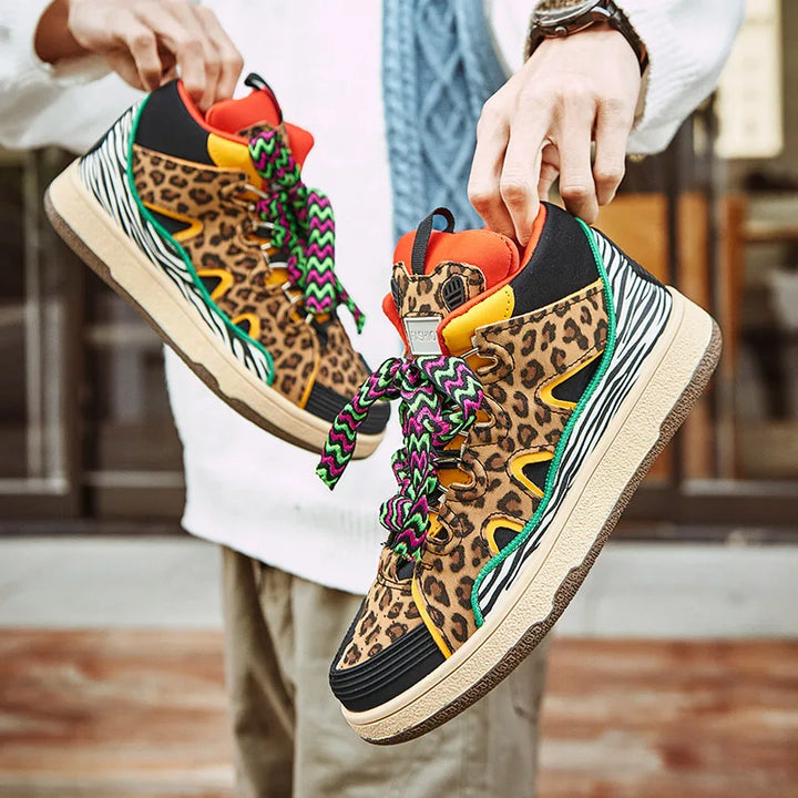 A person holds up a pair of vibrant, animal print shoes featuring leopard print, zebra-striped durable rubber soles, orange and yellow accents, and green-and-purple laces. The lightweight shoes have a bold, wild animal-inspired design.