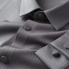 Close-up of a grey business casual shirt with a pointed collar and matte grey snap buttons, highlighting the fabric’s diagonal weave pattern and the details of the button placket and cuffs.