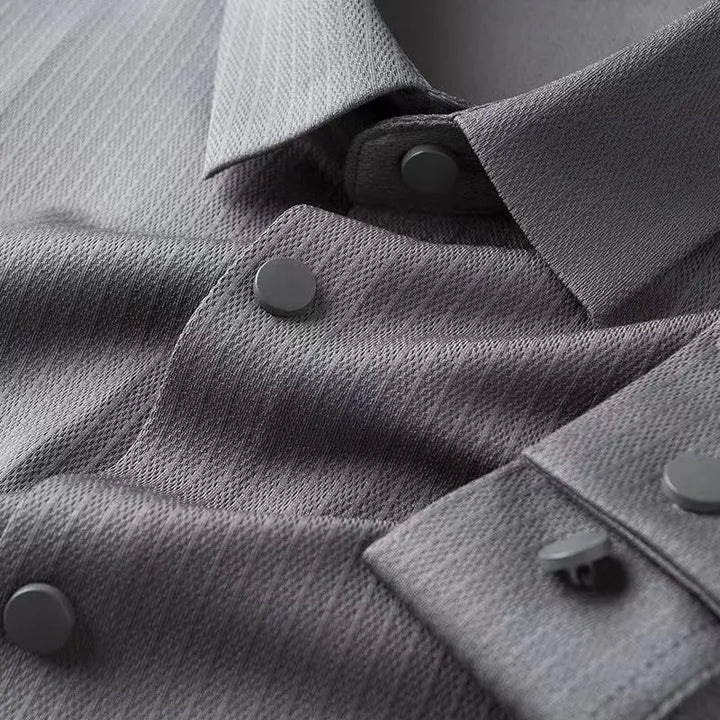 Close-up of a grey business casual shirt with a pointed collar and matte grey snap buttons, highlighting the fabric’s diagonal weave pattern and the details of the button placket and cuffs.