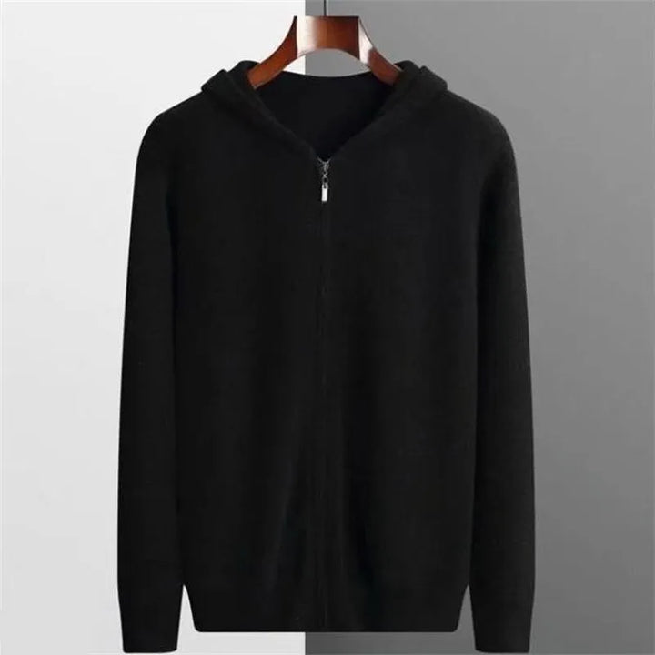 A plain black cashmere hoodie with a hood, displayed on a wooden hanger against a background split into white and gray halves, offering lightweight insulating warmth and timeless style.