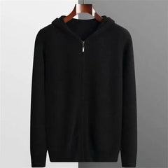 A black lightweight hoodie with a hood, crafted from luxurious cashmere, displayed on a wooden hanger against a background split into white on the left and gray on the right.