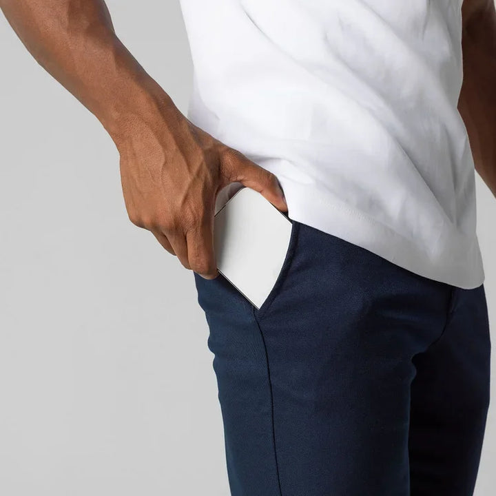 A person wearing a white shirt and blue, slim fit pants slides a white, rectangular object into their front pants pocket.