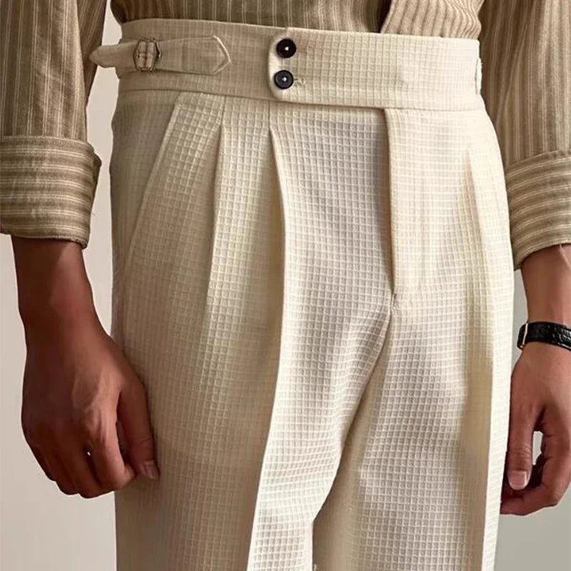 A person wearing high-waisted, cream-colored Havana Fit Slacks with pleats, side tab adjusters, two black buttons, and a beige striped shirt with rolled sleeves.