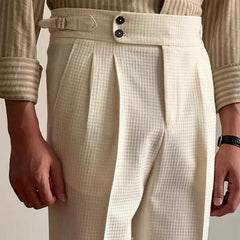 A person wearing high-waisted, cream-colored Havana Fit Slacks with pleats, side tab adjusters, two black buttons, and a beige striped shirt with rolled sleeves.