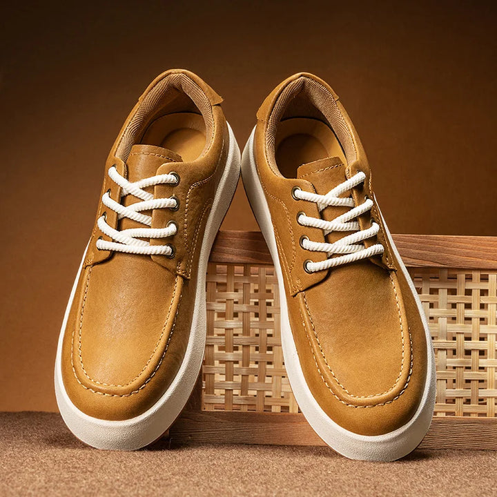 A pair of tan Men's Leather Casual Shoes with white soles and white laces, displayed against a brown background, with one shoe propped up on a wicker panel—perfect breathable walking shoes for everyday style.
