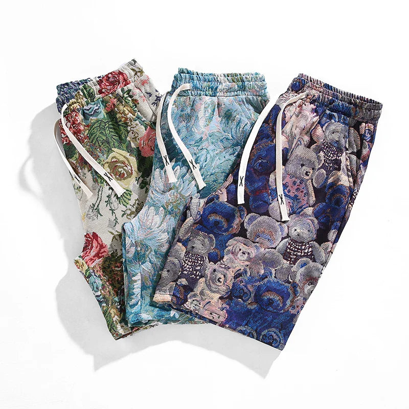 Three pairs of designer shorts with colorful, intricate patterns: one with a pink and green floral design, one with a blue and white floral pattern, and one with blue teddy bear and floral print. All premium quality shorts are laid flat on a white background.