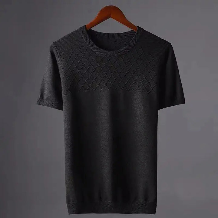 A short-sleeved, dark gray knit sweater with a classic fit hangs on a wooden hanger. The upper chest area features a diamond-pattern texture, while the rest is plain. The background is a simple, neutral gray.