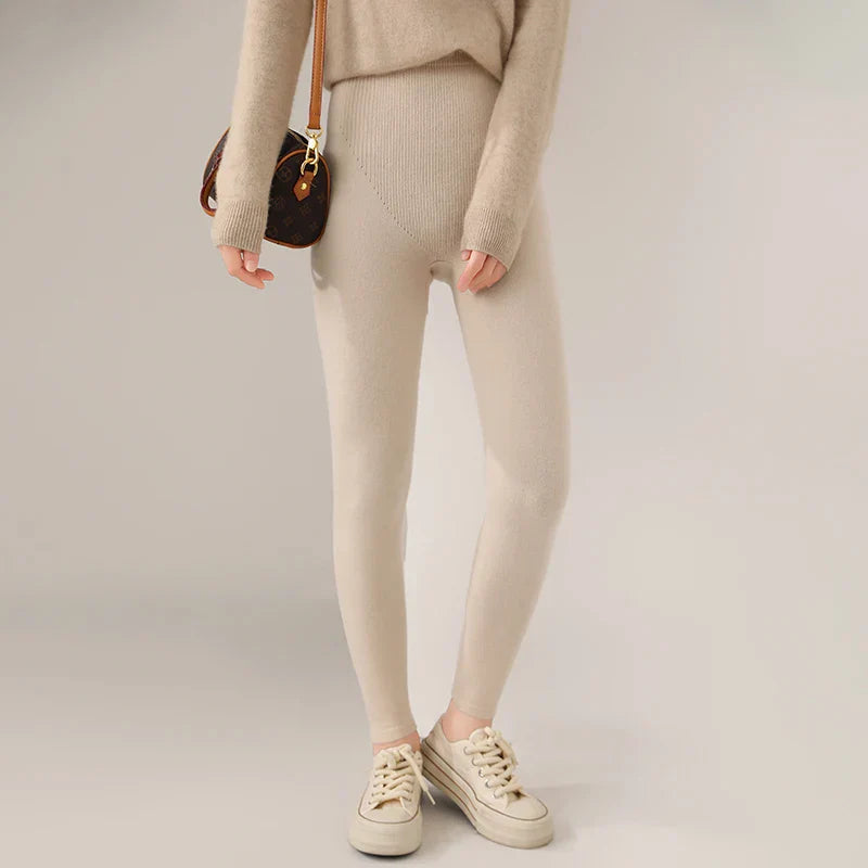 A person wearing high-waisted leggings and a matching beige sweater, white sneakers, and carrying a brown shoulder bag stands against a plain light background. Their head and lower arms are out of frame.