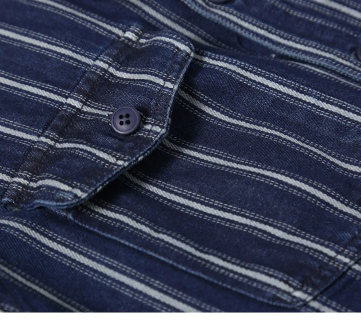 Close-up of a blue denim vintage button-up shirt with white horizontal stripes, a buttoned flap pocket, and visible stitching details crafted from heavyweight cotton.
