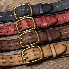 Five vintage-inspired belts in black, dark red, brown, dark brown, and tan are laid out on a wooden surface, each featuring a large gold buckle and visible stitching for that classic double needle buckle belt look.