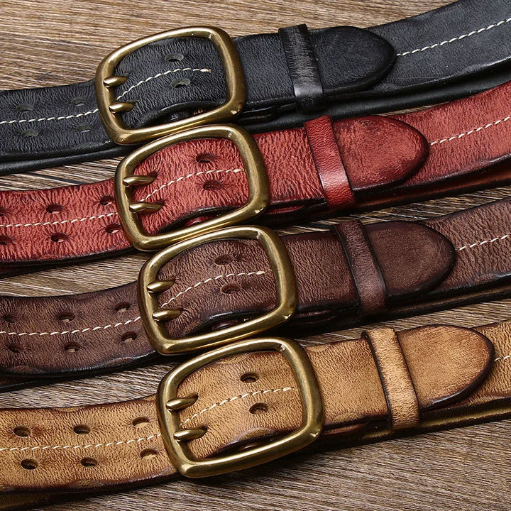 Five vintage-inspired belts in black, dark red, brown, dark brown, and tan are laid out on a wooden surface, each featuring a large gold buckle and visible stitching for that classic double needle buckle belt look.