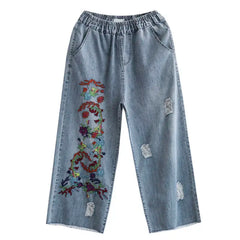 Light blue loose-fitting denim wide-leg jeans with an elastic waistband, front pockets, distressed patches, and a bold retro embroidery floral design running vertically down one leg.
