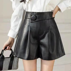 A woman wears high waist black faux calfskin leather shorts with a striking button detail, paired with a white blouse. She carries a small black and white checkered handbag.