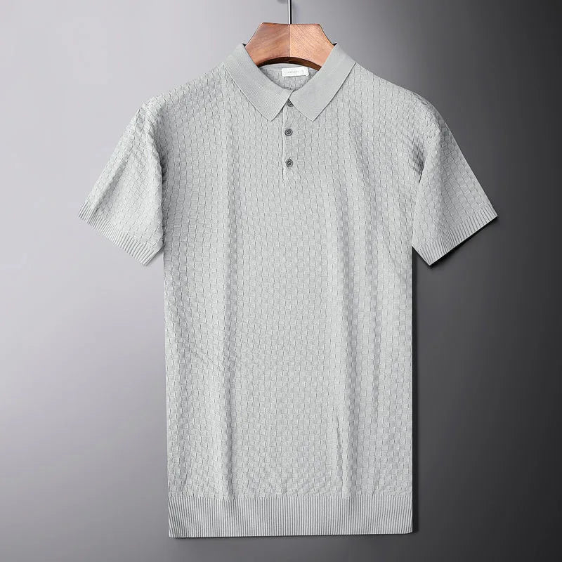 A light gray short-sleeve knit polo shirt with a subtle waffle jacquard pattern hangs on a wooden hanger against a gray background. The shirt features a collar and a three-button placket.