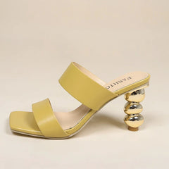 A stylish yellow sandal with two wide straps, a square toe, and a sculpted heel made of stacked metallic spheres. Crafted from premium leather, it features FASHION on the insole for an eye-catching finish.