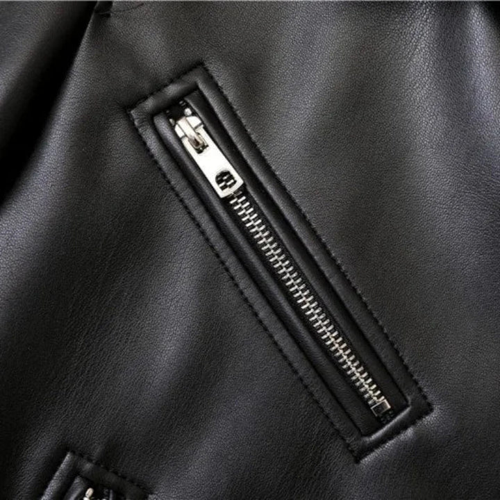 Close-up of a black leather jacket featuring a shiny silver zipper, sewn diagonally with visible stitching around the zipper area, highlighting the texture and details of the material.