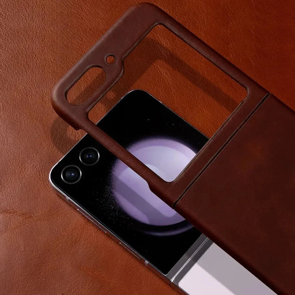 A genuine leather phone case sits on a brown leather surface, partially covering a Samsung Galaxy Z Flip with dual rear cameras and visible hinge, offering both elegance and shockproof protection.